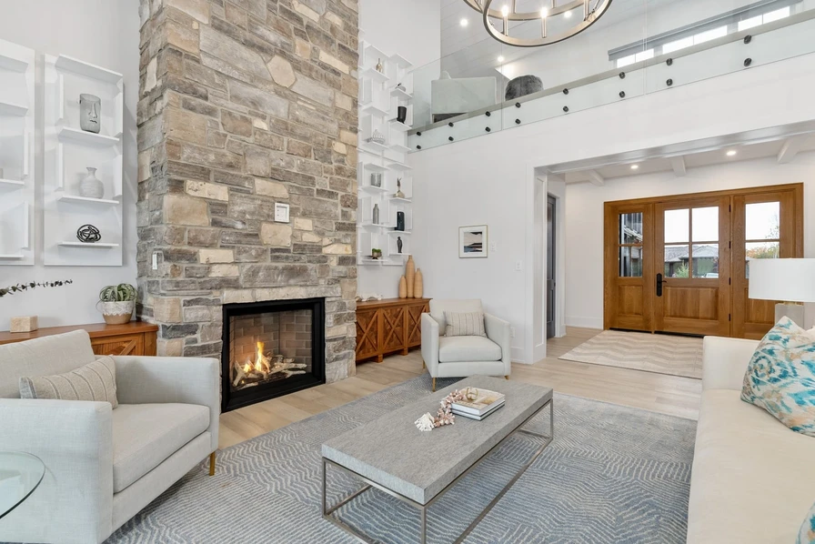 A welcoming living room with a stone fireplace, white shelving and a wood front door.