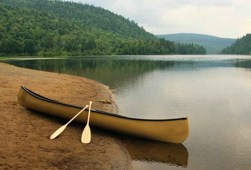 A yellow canoe and paddles on a sandy lakeshore.