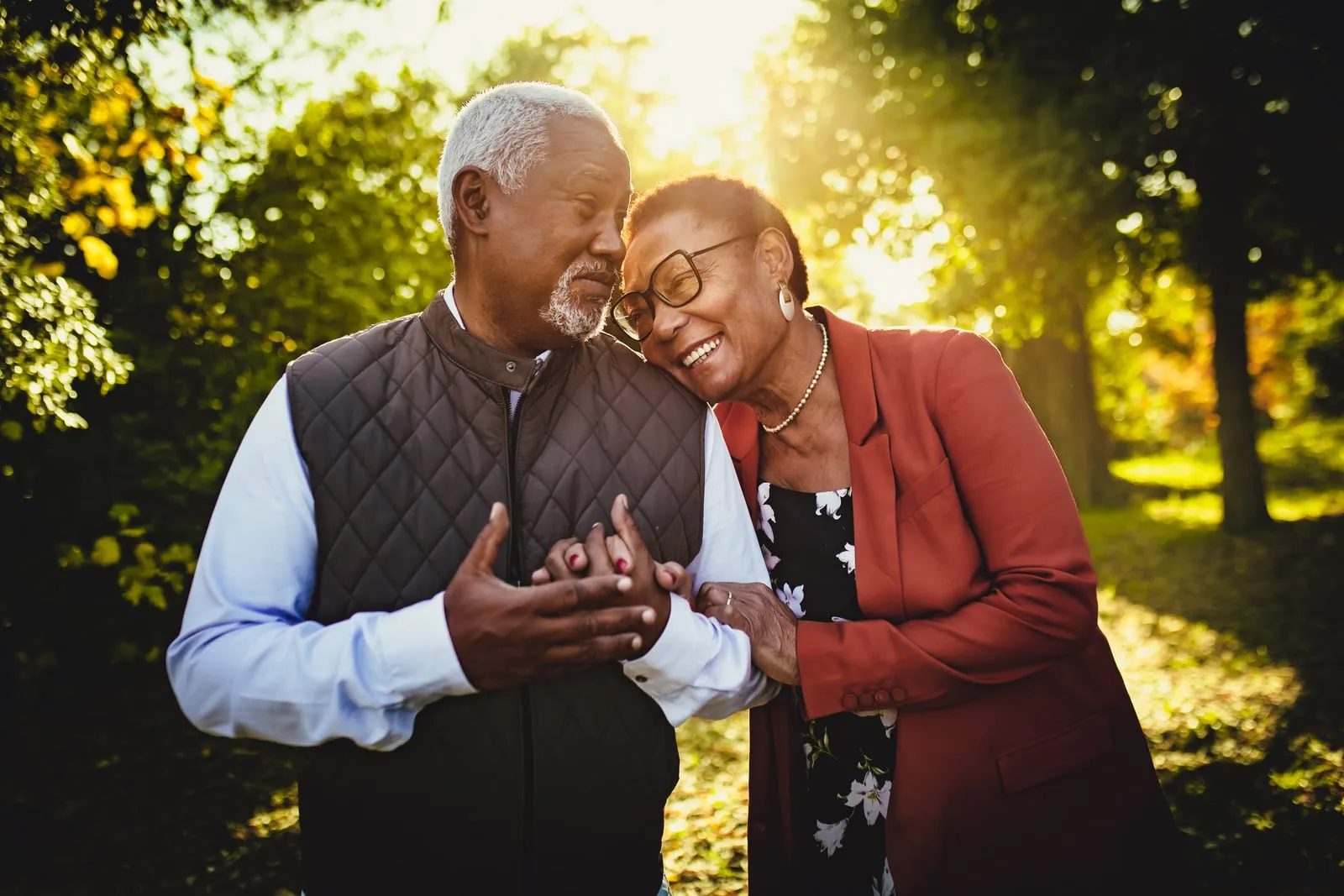Smiling senior couple leaning together beneath sunlit autumn trees.