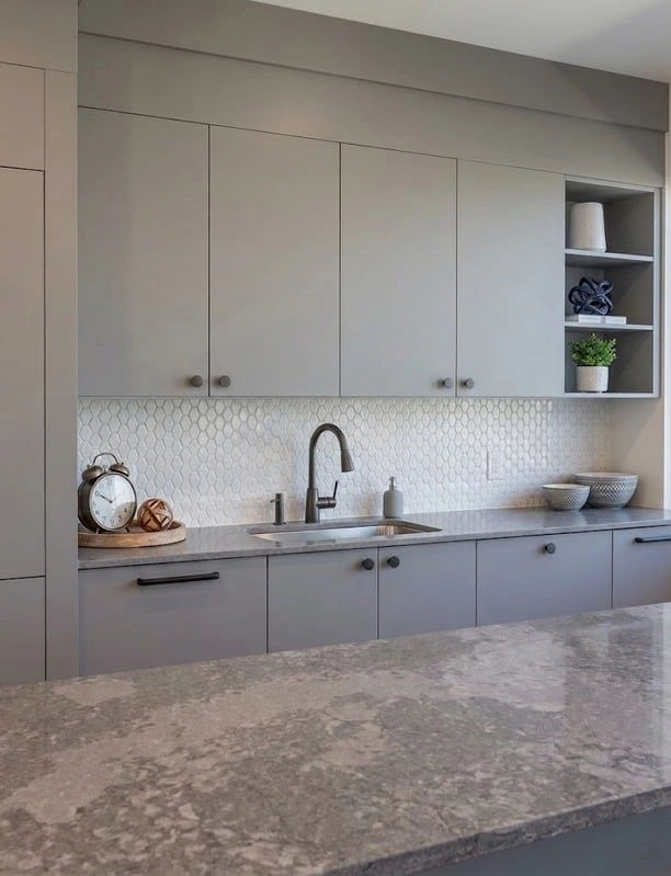 Grey kitchen cabinetry with a stone countertop and backsplash.